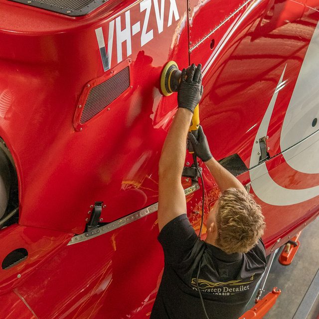 Detailer machine polishing a red helicopter inside the hangar