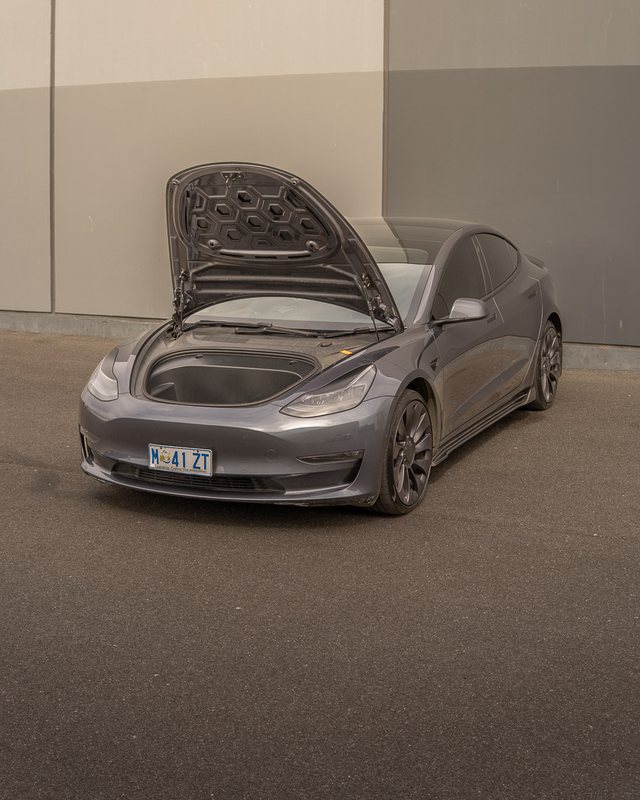 Grey 2022 Tesla Model 3 Performance with the front boot open, parked against a warehouse wall